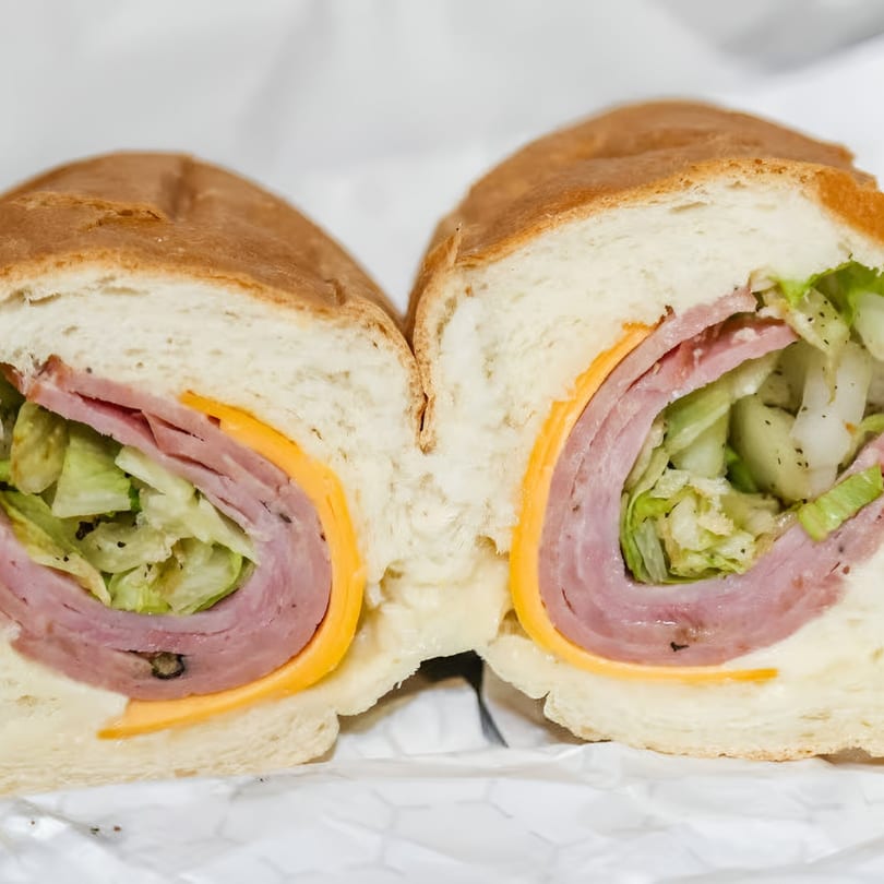 A sliced sub sandwich with ham, cheese, and lettuce on a white background.