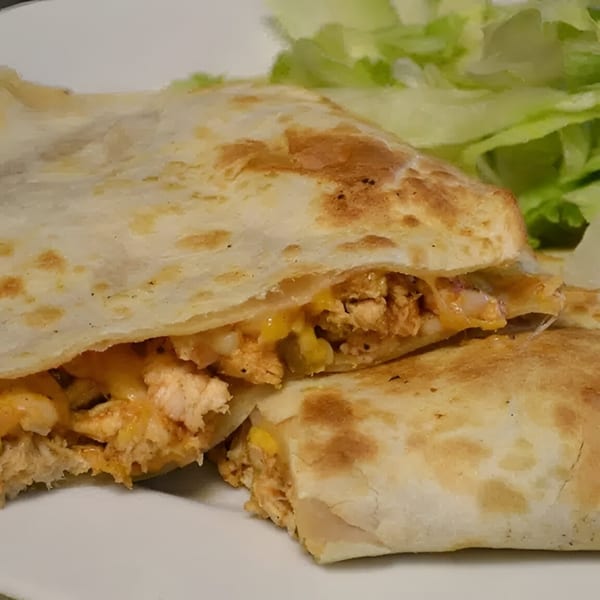 A chicken quesadilla with melted cheese and corn, served with a side of fresh lettuce.