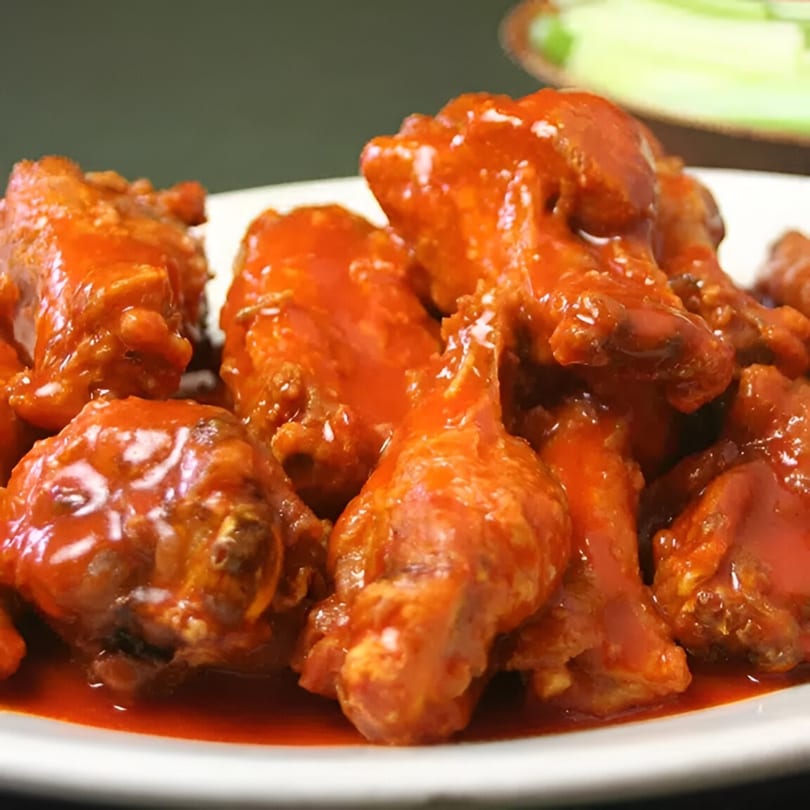A white plate piled high with glistening, saucy buffalo chicken wings from Wings Things & Pizza.