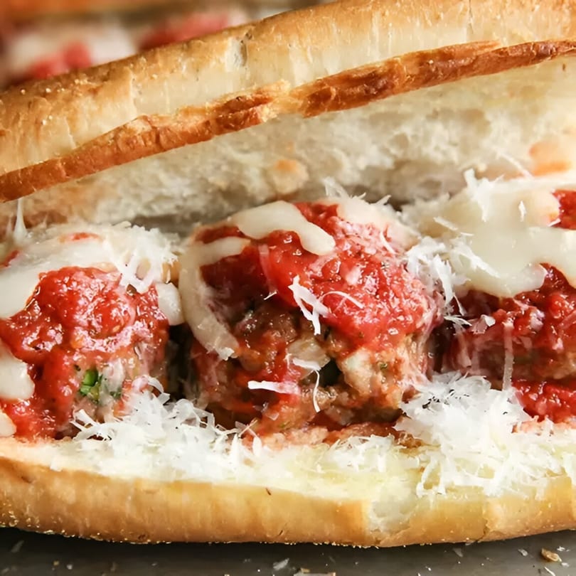Close-up of a meatball sub with marinara sauce, melted mozzarella, and grated Parmesan cheese.